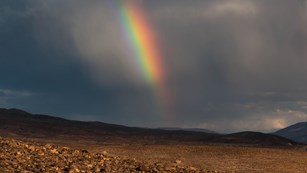 A rainbow in the distance in a desert landscape. 