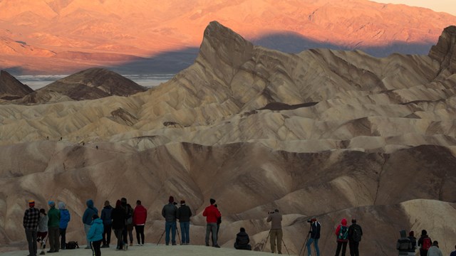 A group of photographers stand on a ridge photographing the sunrise on the desert hills.