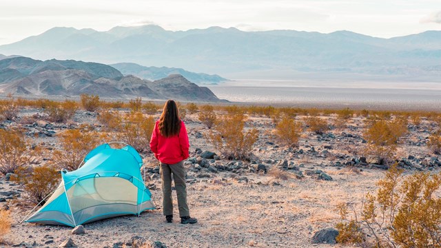 a camper stands next to a tent in desert scenery