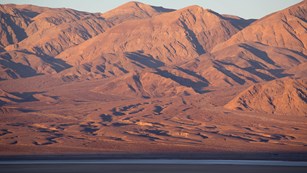 Warm, pink, sunrise light on distant desert mountains.