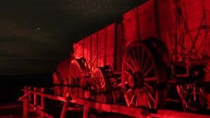 Night image with red light illuminating a wooden fence and historic wooden twenty mule team wagon.