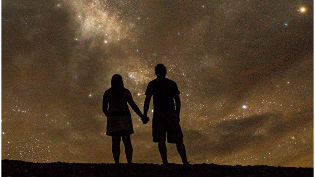 Night image of two people holding hands looking at the Milky Way.