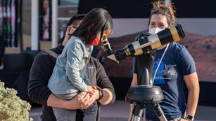 A scientist helps a child look through a telescope with a solar lens.