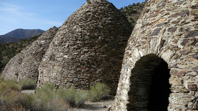 Four masonry bee-hive shaped structures approximately 30ft tall with low green shrubs in front.