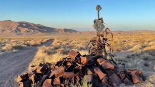 Pile of historic rusty cans and metal artifacts with a desert landscape in evening light.