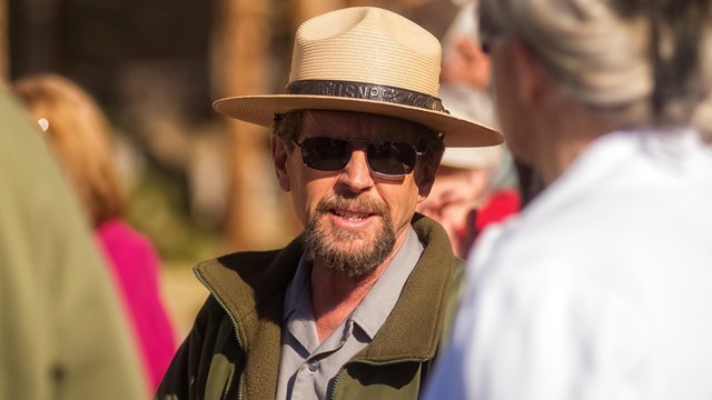 a ranger in a hat speaks with visitors