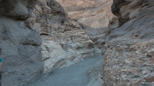 A path leads through a narrow, smoothly eroded, rocky canyon. 