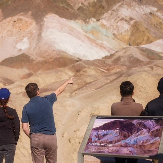 Four visitors pointing at a colorful landscape known as Artists Palette.