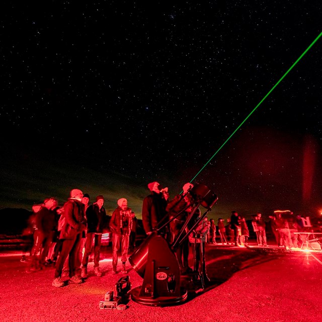 Various individuals use red light at night and point green laser into sky.