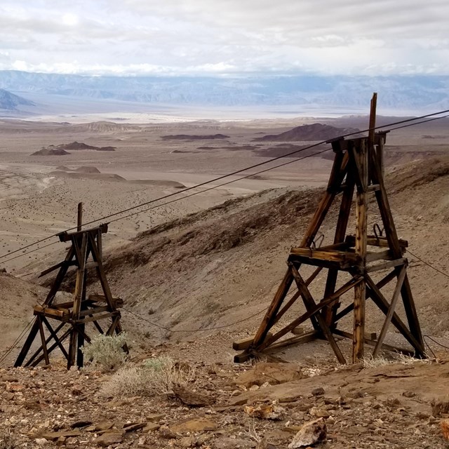 Two weathered wooden towers supporting cables for transporting ore buckets.