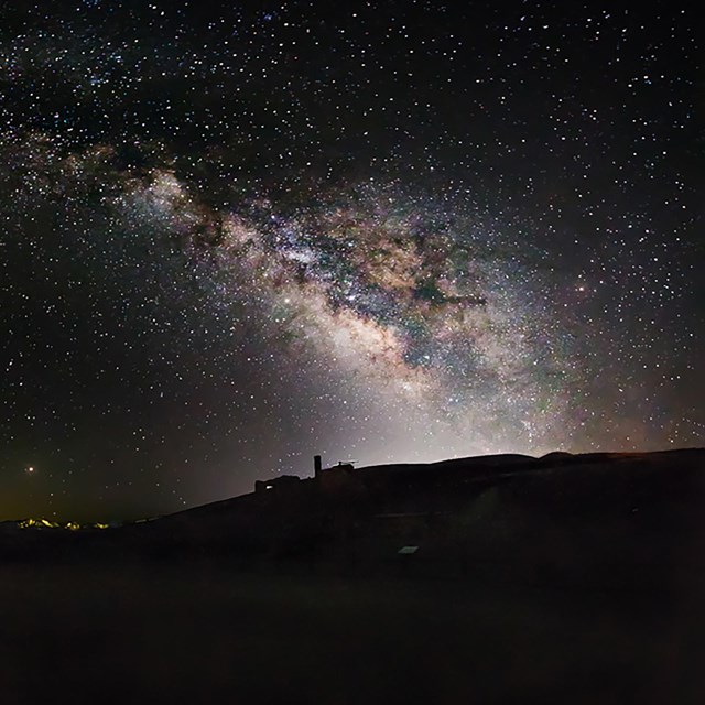 The milky way shines bright in the sky over black mountain silhouettes.