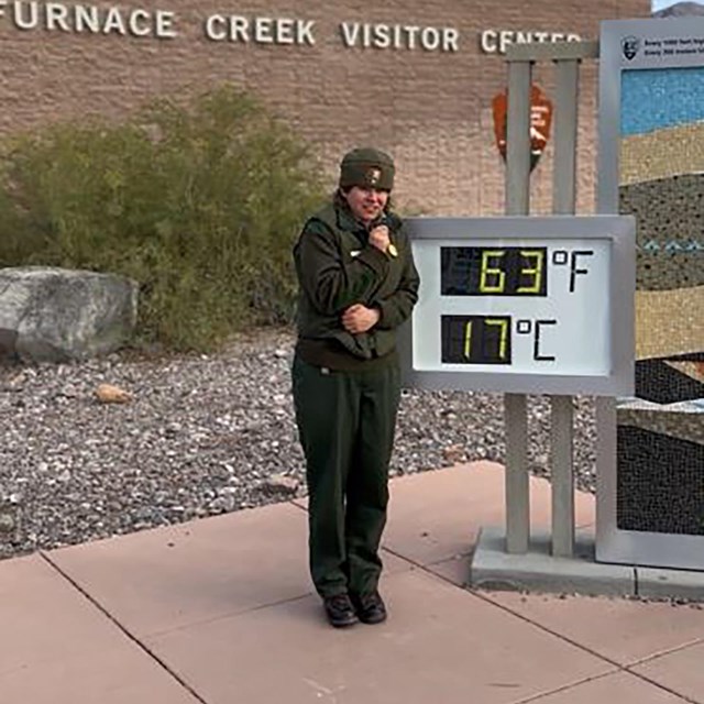 Ranger in uniform standing outside a brick building in front of a large digital thermometer.