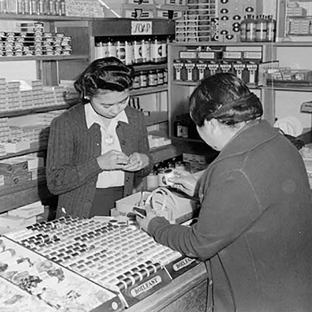 A black and white image of two women on opposite sides of a counter, standing in a store.