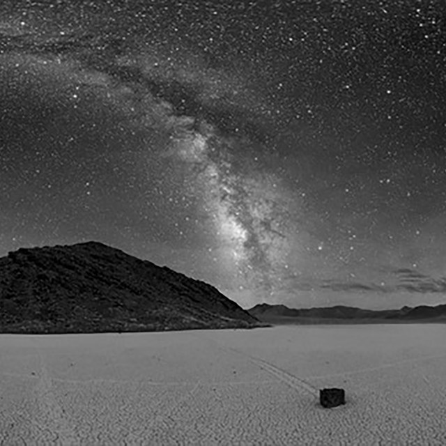 A grayscale landscape image of a playa with a rock seemingly moving across the ground.