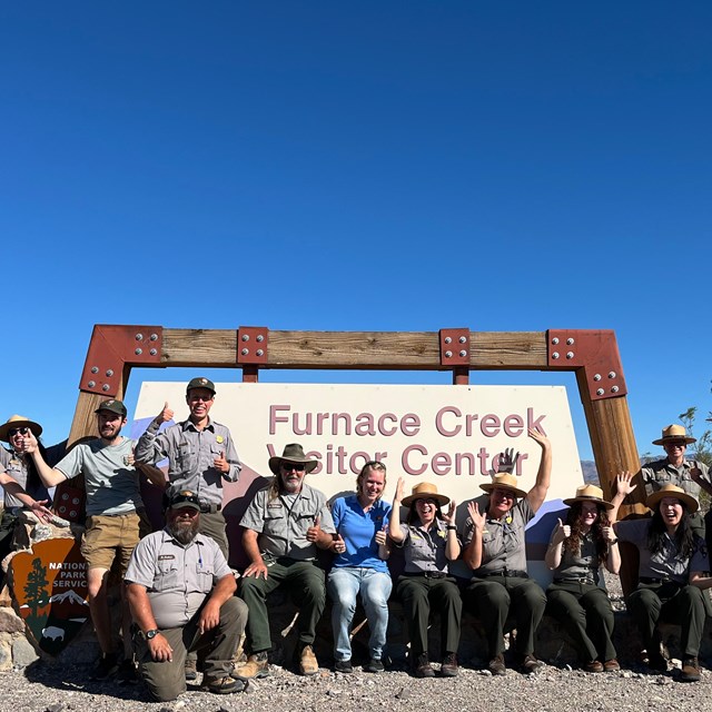 a group of smiling people in Park Service uniforms in front of a National Park sign