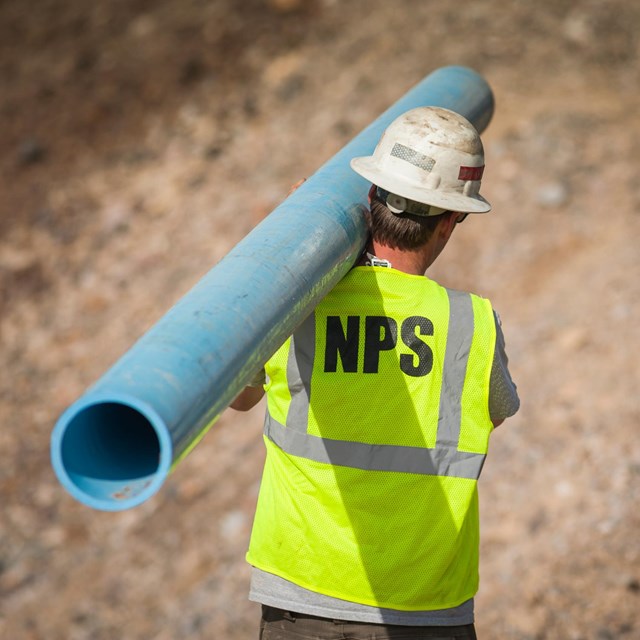 A National Park Service employee carries a replacement pipe segment.