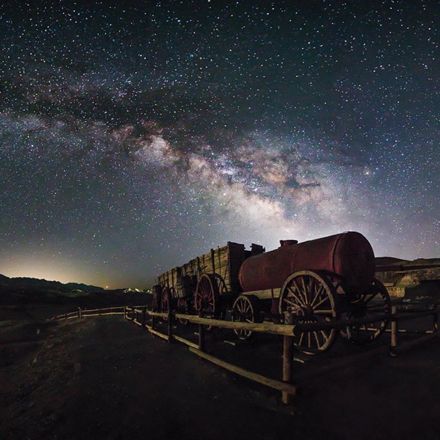 A dark sky filled with stars over a wooden and metal historic wagon.