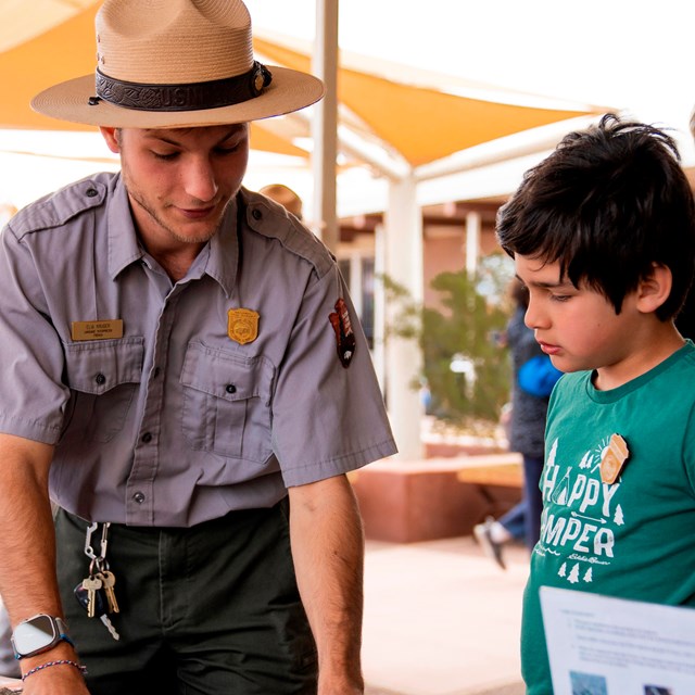 Uniformed ranger goes through a Junior Ranger book with a child wearing a green shirt.