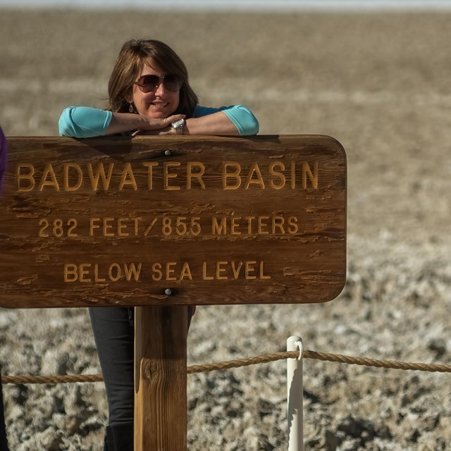 A child takes a picture of a woman at the wooden Badwater sign reading: 282 feet below sea level