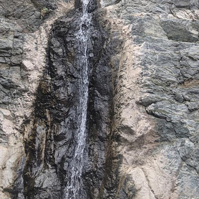 A thin stream of water flows over a tall rocky ledge. Text on the image reads: W is for Waterfall.