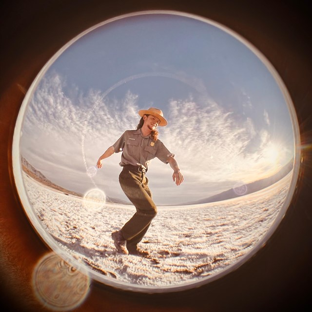 A uniformed ranger poses on Badwater Basin salt flat in Death Valley through a fish eye lens.
