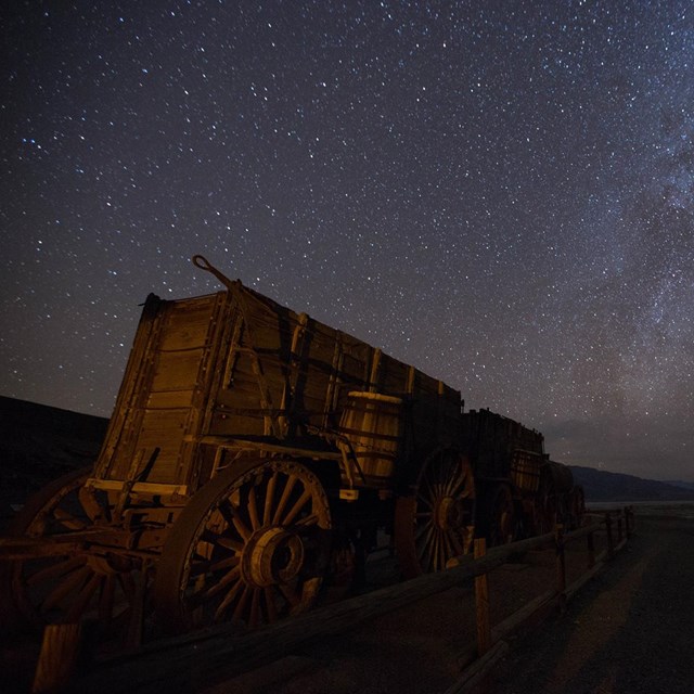 A nighttime photo showing an illuminated historic wagon with the milky way rising above it.
