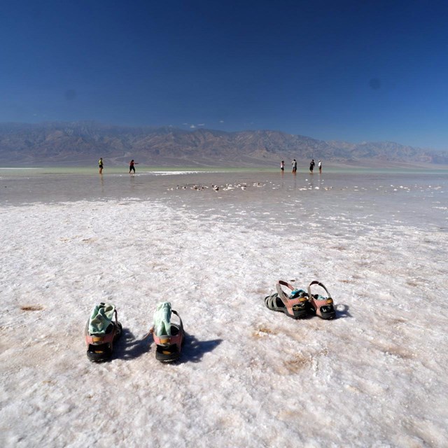Sandals on top of a salt flat with visitors enjoying a shallow lake in the middle ground of the imag