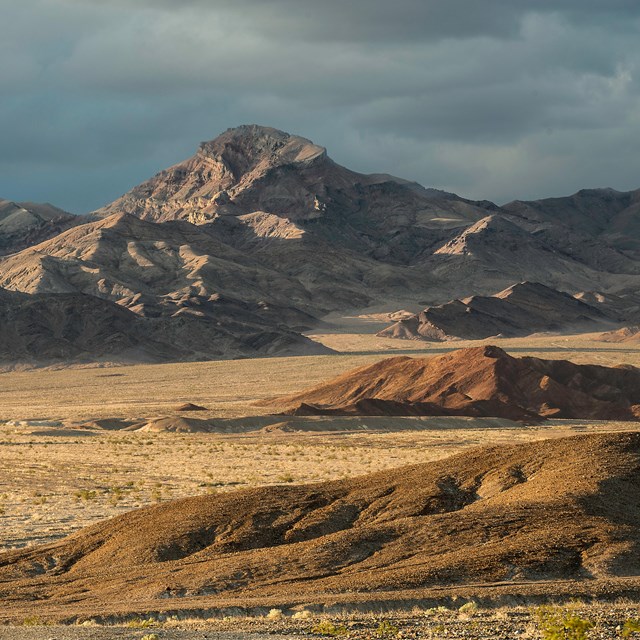 The image showcases multiple geological layers, from rocky hills in the foreground to high mountains