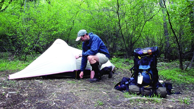 A man sets up a tent with a larger backpack off to the right side. NPS Photo