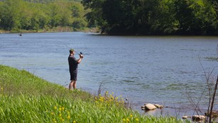 A man in a baseball hat casts a line into the Delaware river