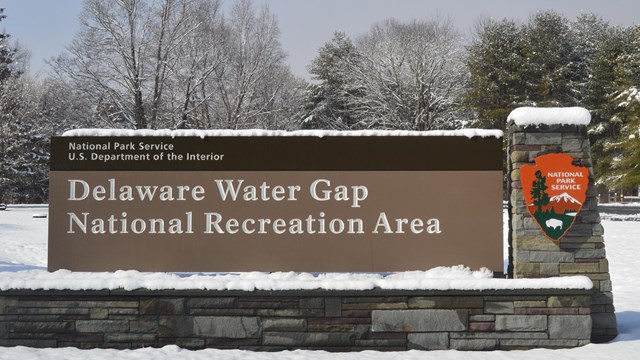The park entrance sign with a layer of snow all around and on it.