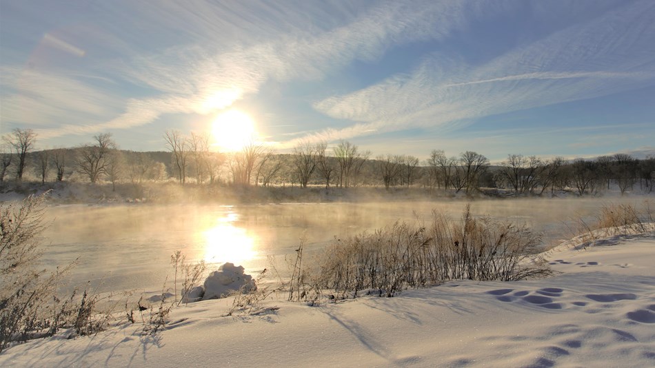 Icy Delaware River with trees in background and sun rising behind