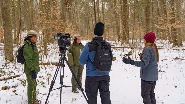 Two Rangers stand with a news crew on a snowy trail.