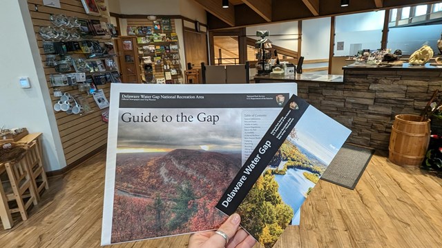 Two brochures being held out with the visitor center desk in the background.