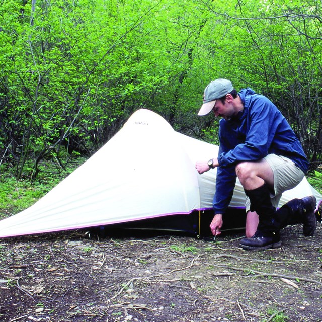A man sets up a tent with a larger backpack off to the right side. NPS Photo