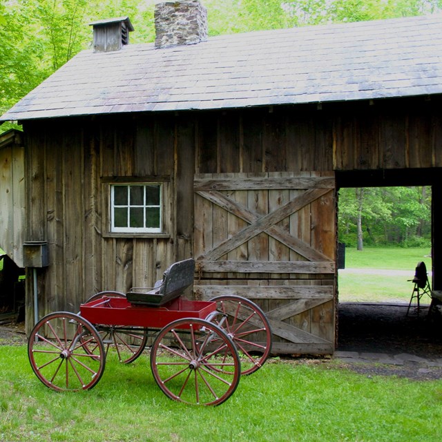A wooden barn with a slate tile roof and a horse drawn buggy in front