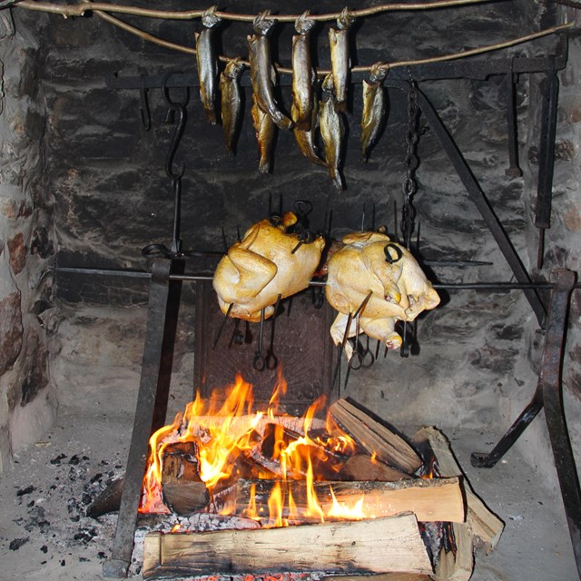 Chickens grilling in a stone fireplace with wood burning gently below