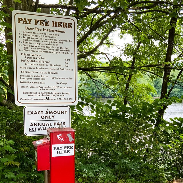 A red metal fee box at a park river access.