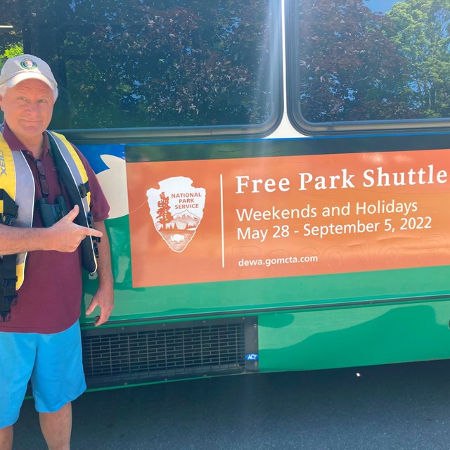A volunteer stands next to a bus with a free park shuttle decal.