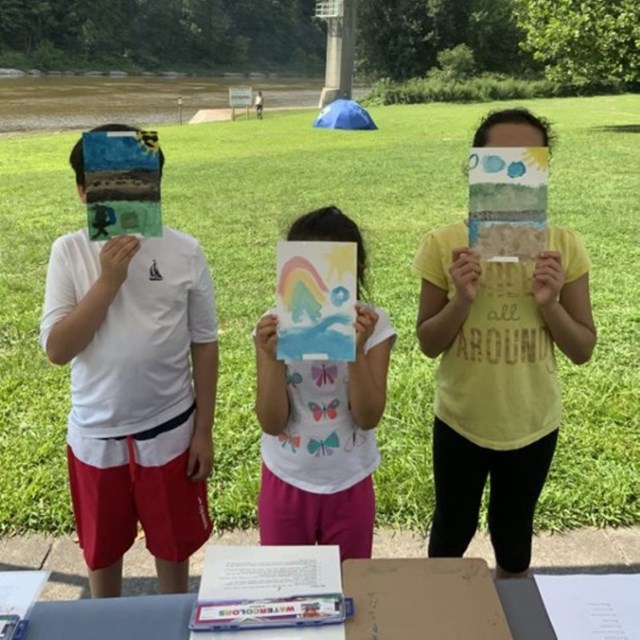 Three children stand with painted pictures in front of their faces.