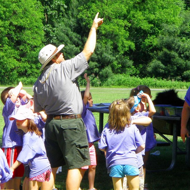 A ranger points at the sky as a group of students follow his gaze.