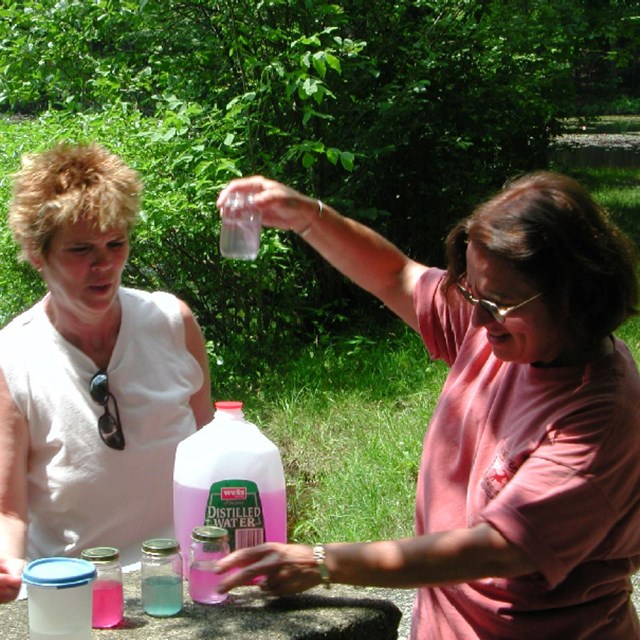Two teachers work on a demonstration in front of a pond.