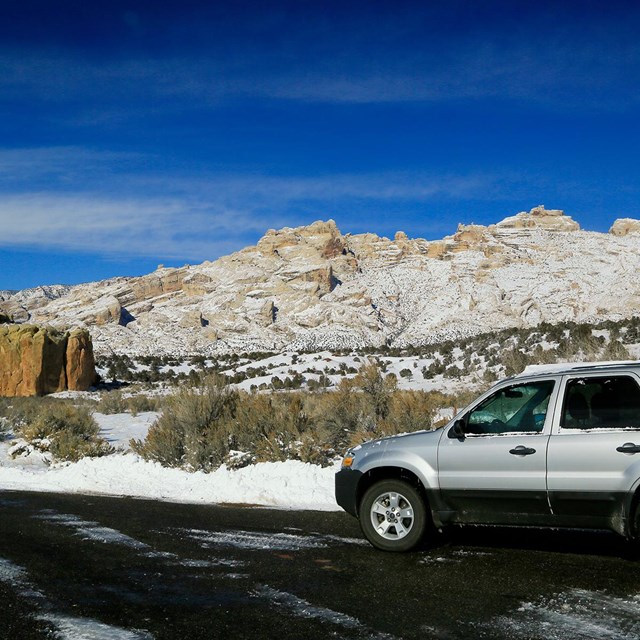 Silver vehicle sitting on road with rocky mountains covered in snow in the background