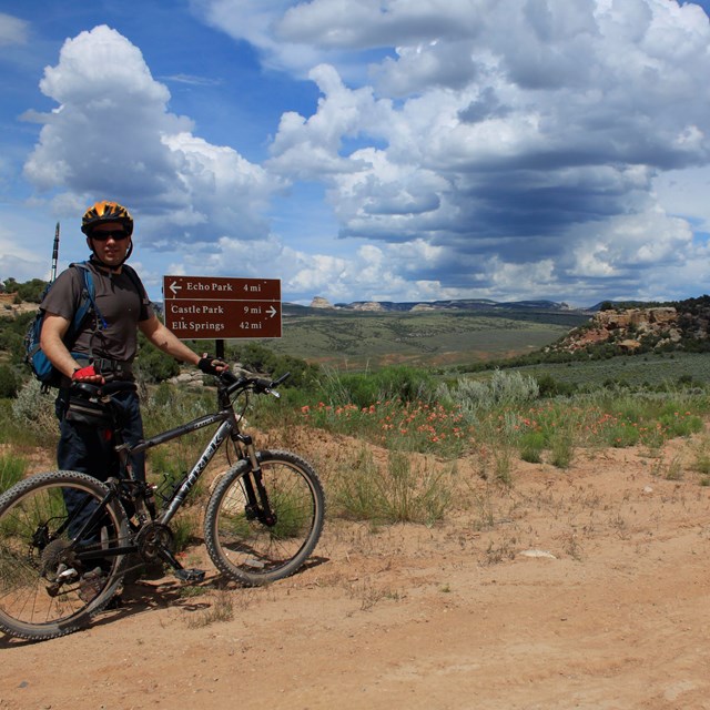 Man holding a bike beside a dirt road.