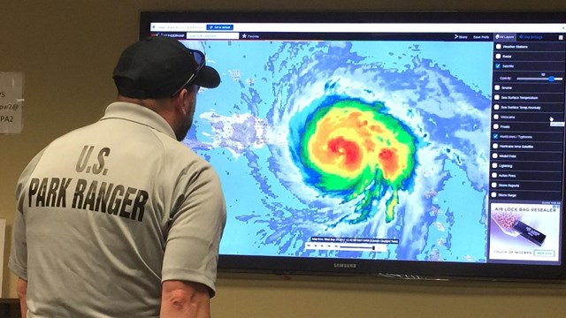 Park ranger looking at radar image of hurricane on television