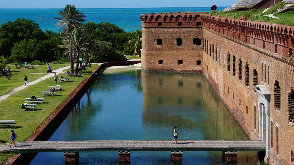 A brick structure surrounded by water, a walkway, and vegetation. 