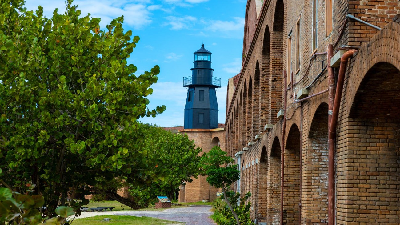 A brick structure surrounded by water, a walkway, and vegetation. 