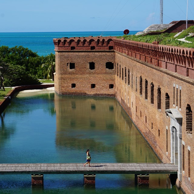 A brick structure surrounded by water, a walkway, and vegetation. 