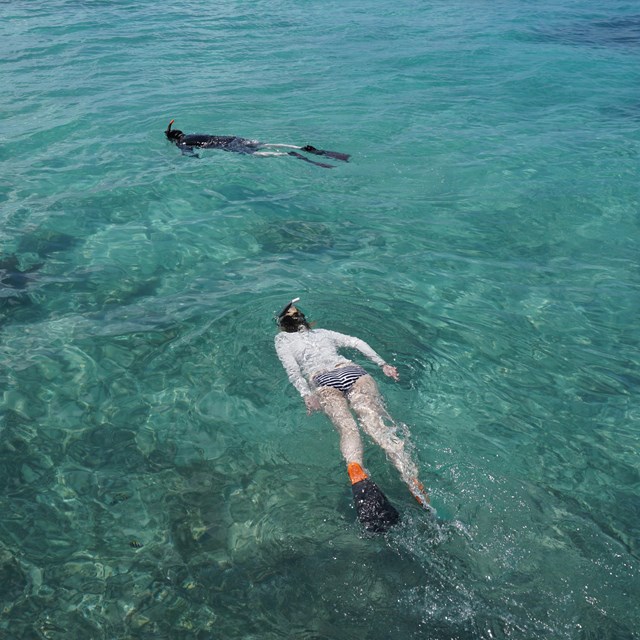 two people swimming in the ocean next to a brick walkway