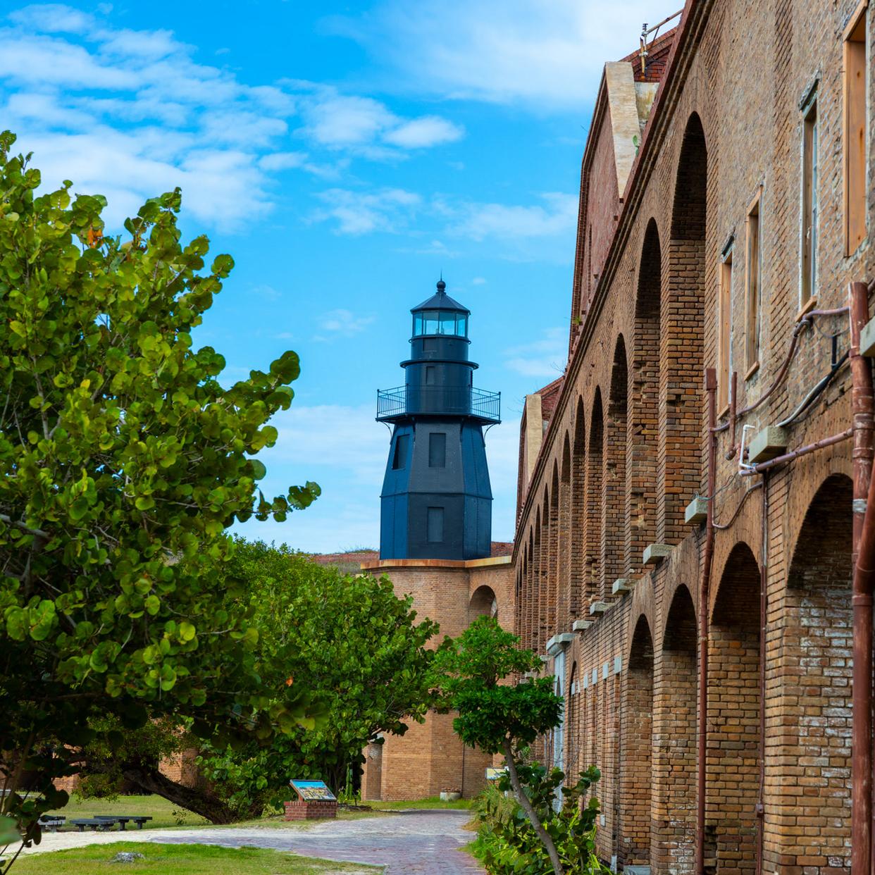 A brick structure surrounded by water, a walkway, and vegetation. 